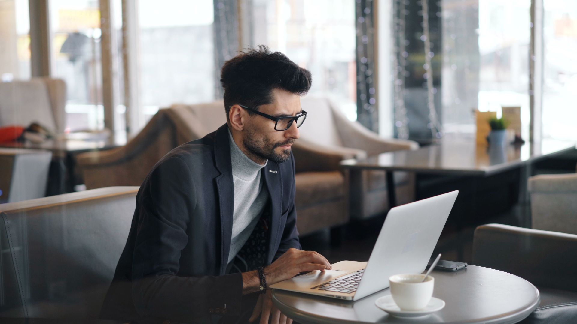 Focused businessman working on a laptop in a stylish café, drinking coffee.