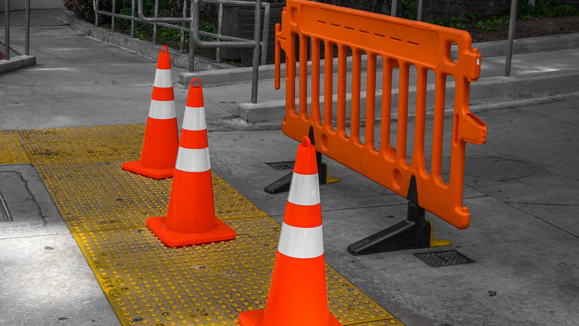 Bright orange traffic cones and a barrier on a city sidewalk.