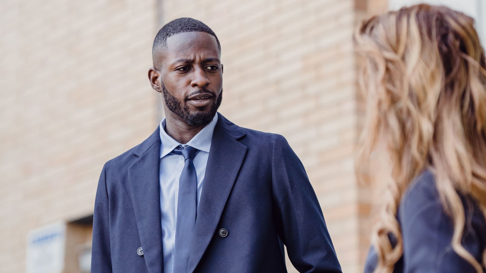 Two business professionals engage in conversation outside a building, wearing formal attire.