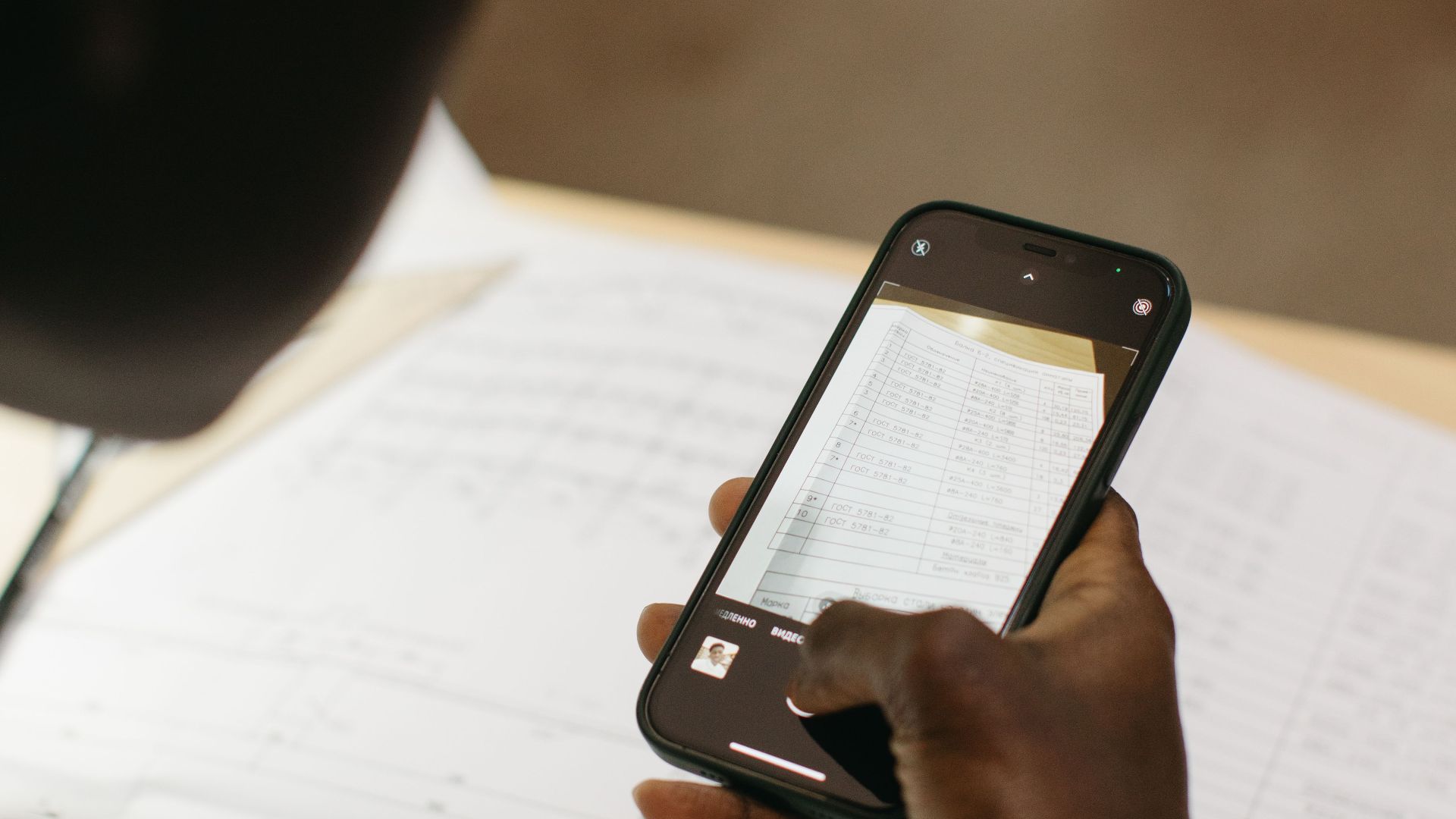 Close-up of person using smartphone to scan document, emphasizing mobile technology utilities in the workplace.