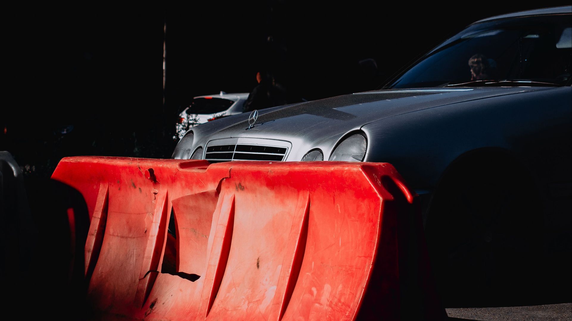 A red barrier obstructing a silver car under dramatic lighting, creating a vivid street scene.