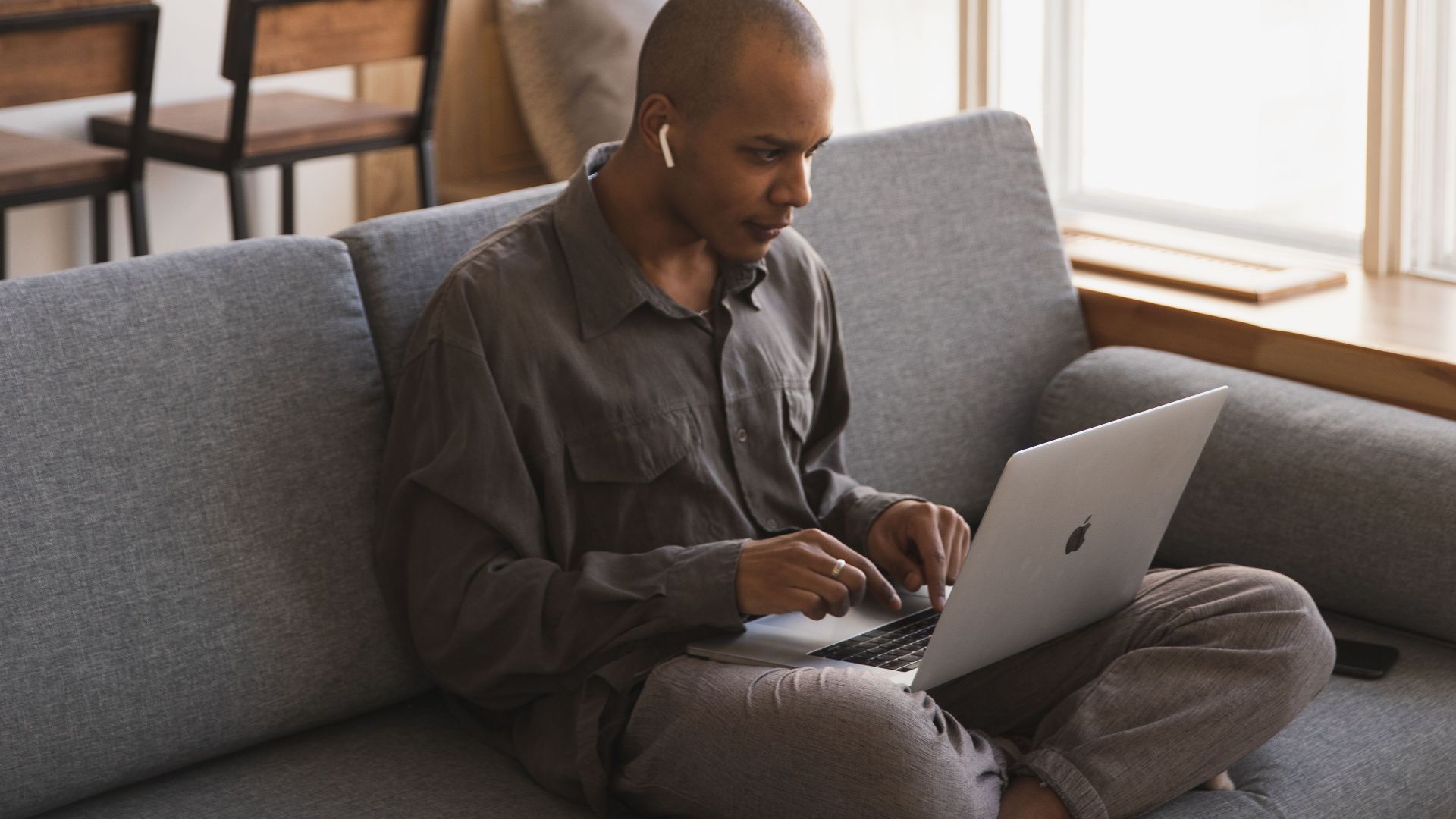 Man sitting on couch working on a laptop in a cozy home setting, embodying remote work lifestyle.