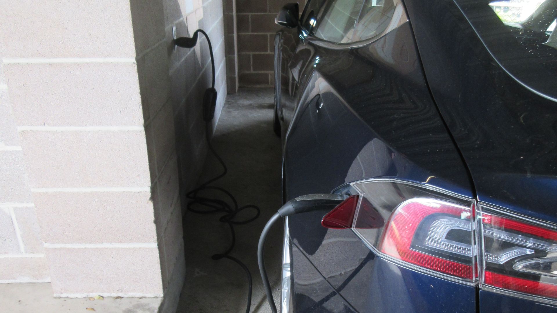 Tesla Model S in parking garage in Uptown New Orleans, plugged into wall outlet.