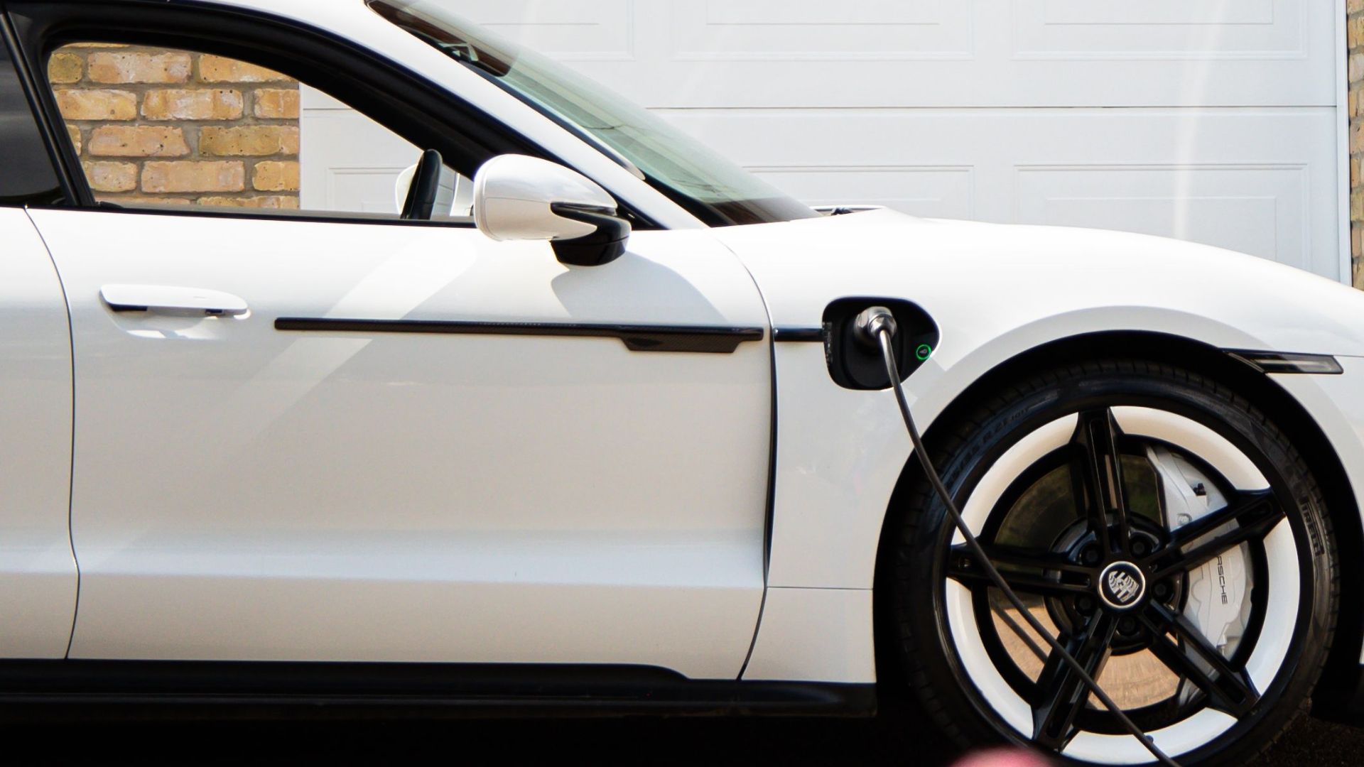 A white electric car charges at a home station with solar panels.