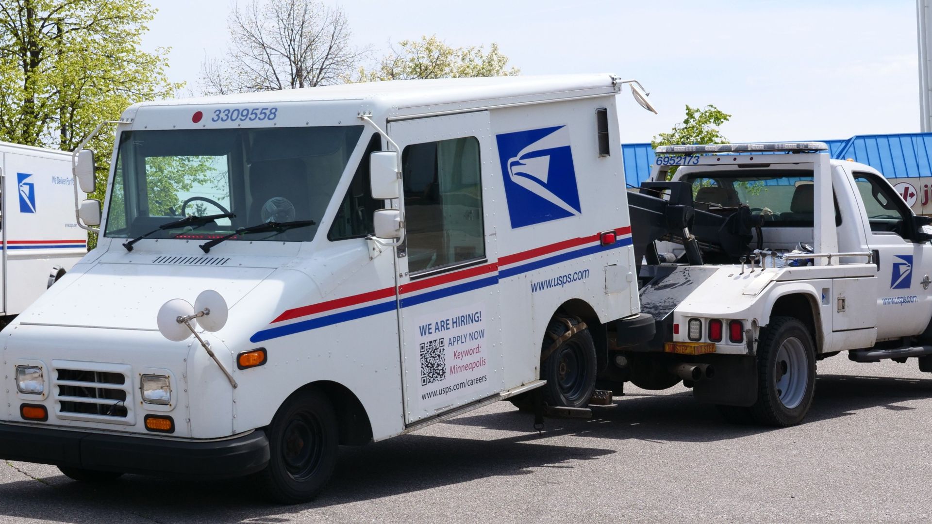 A United States Postal Service (USPS) mail truck is being towed outdoors on a clear day.