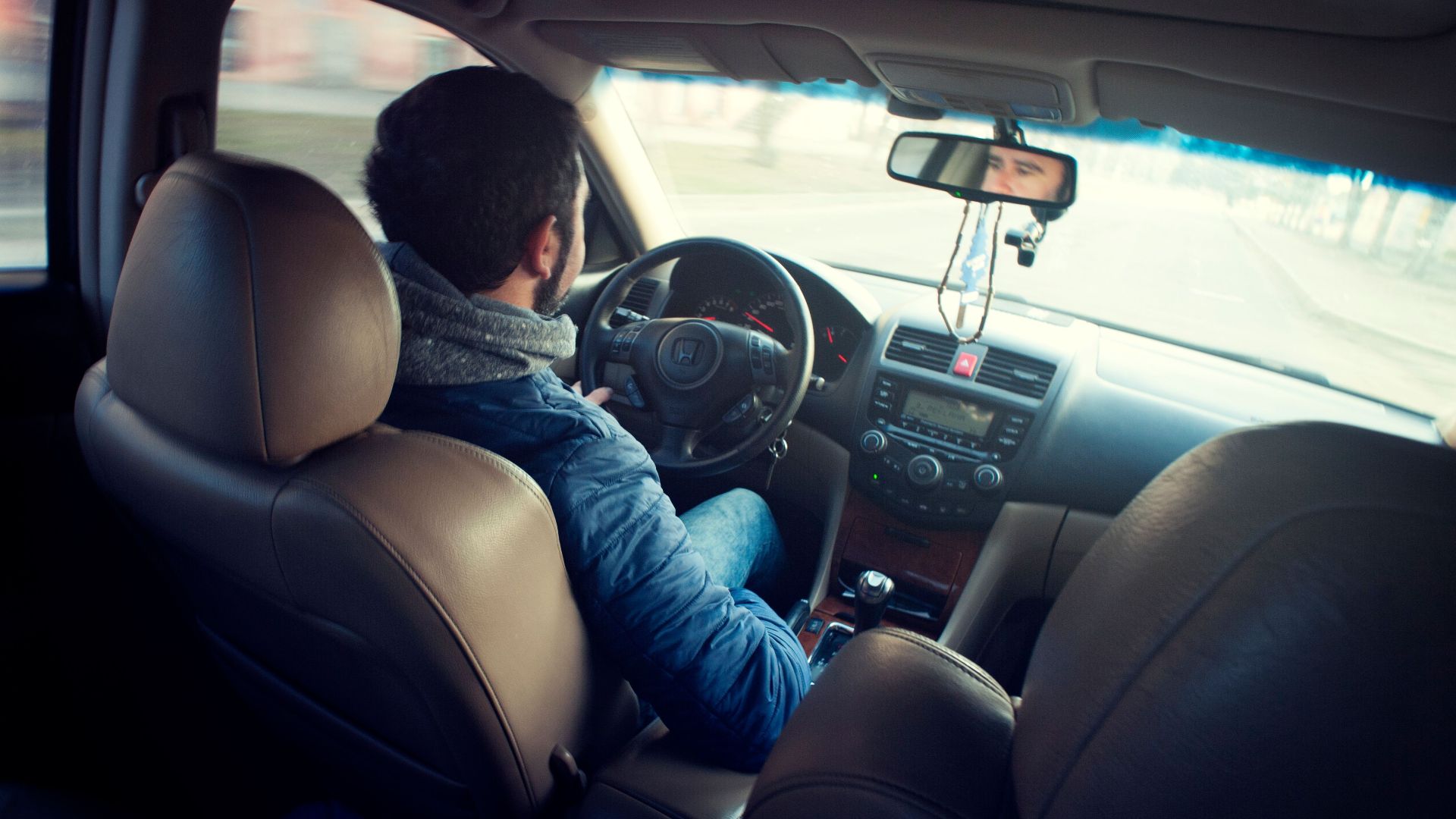 A man driving a car with focus on interior, dashboard, and steering wheel, captured from the backseat.