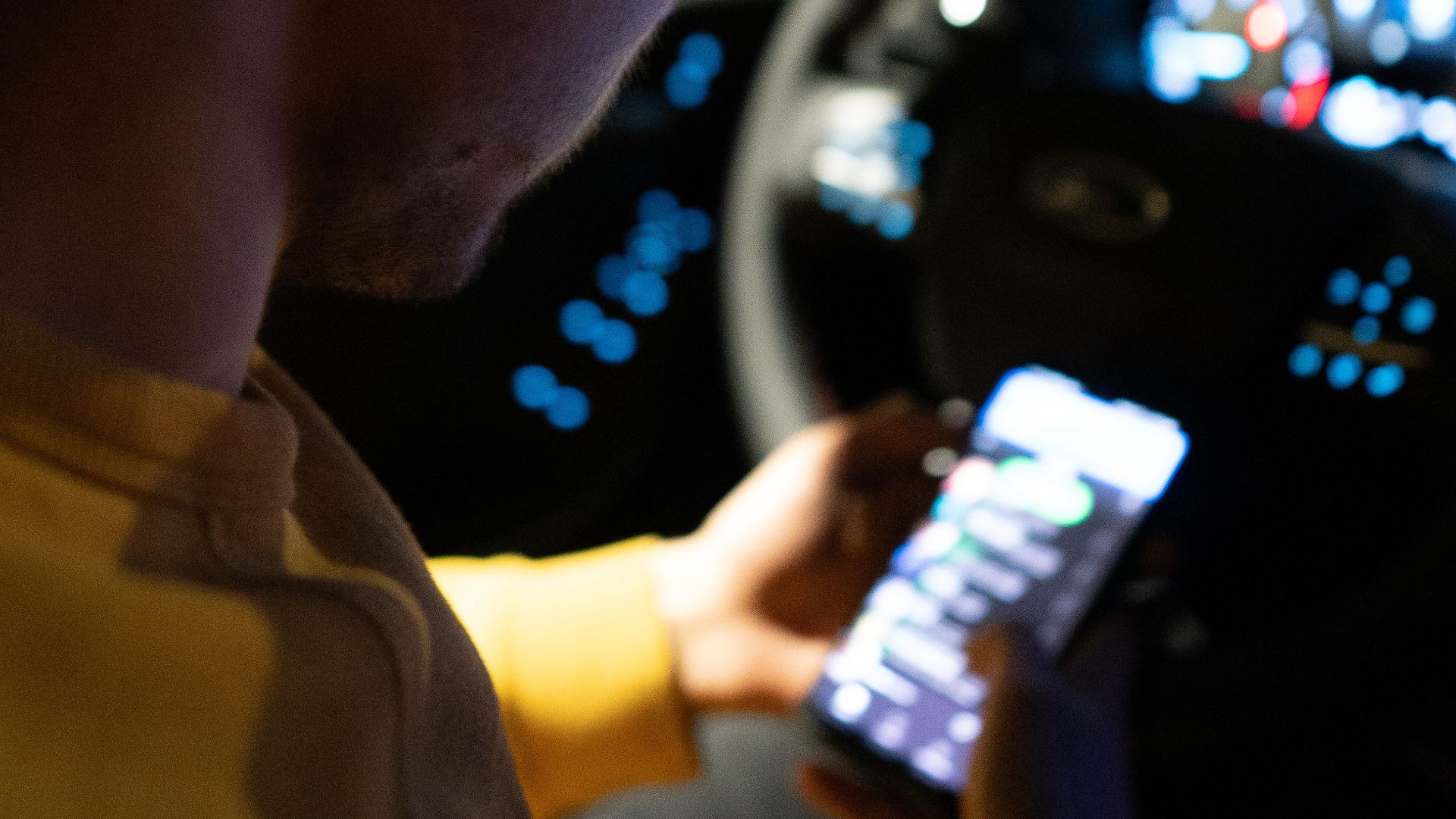 Person using a smartphone inside a car at night, focusing on technology and safety.