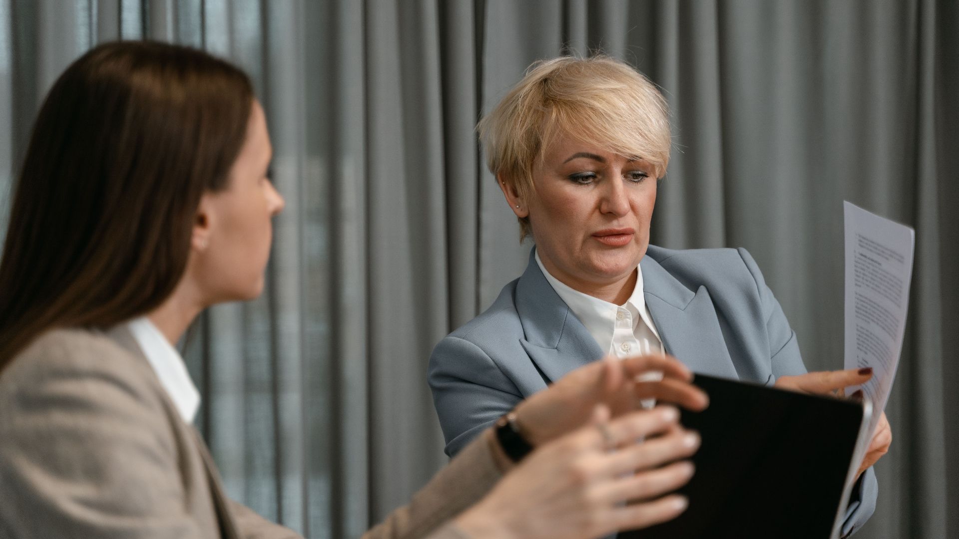 Two women discussing documents in a corporate meeting.