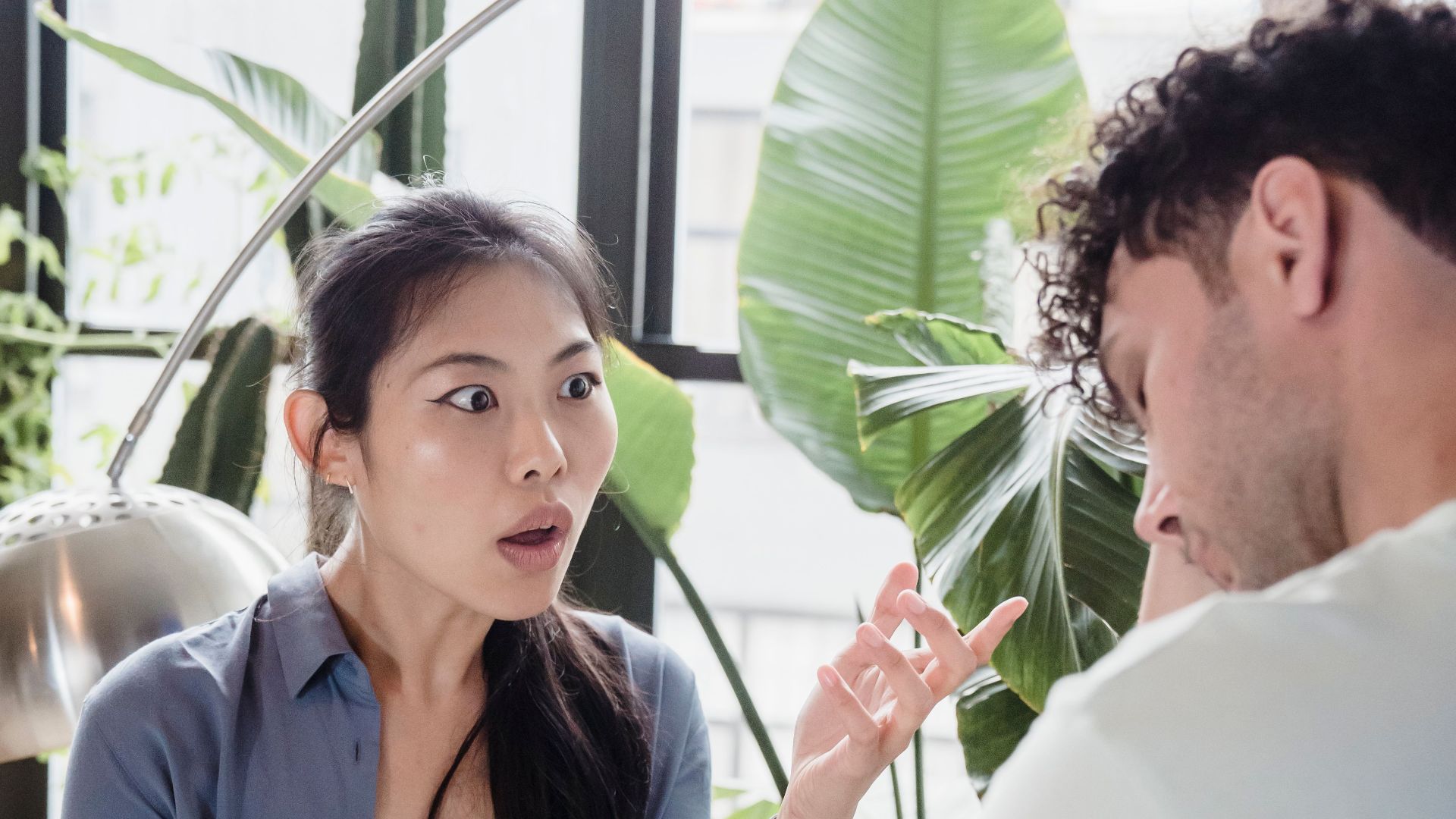 A couple engaged in a heated discussion in a room with lush indoor plants.