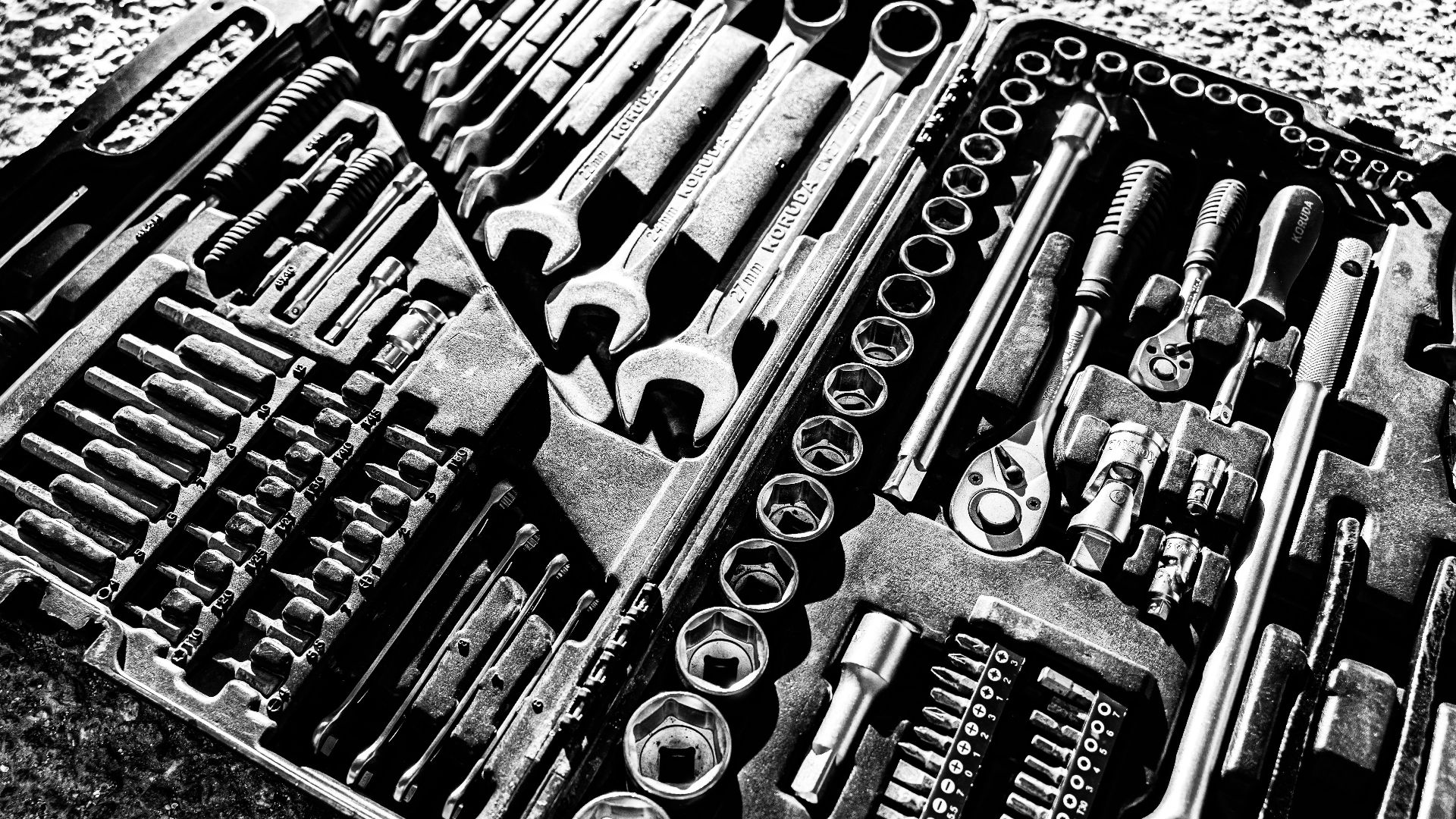 Close-up black and white photo of a complete wrench and socket tool set within a toolbox.