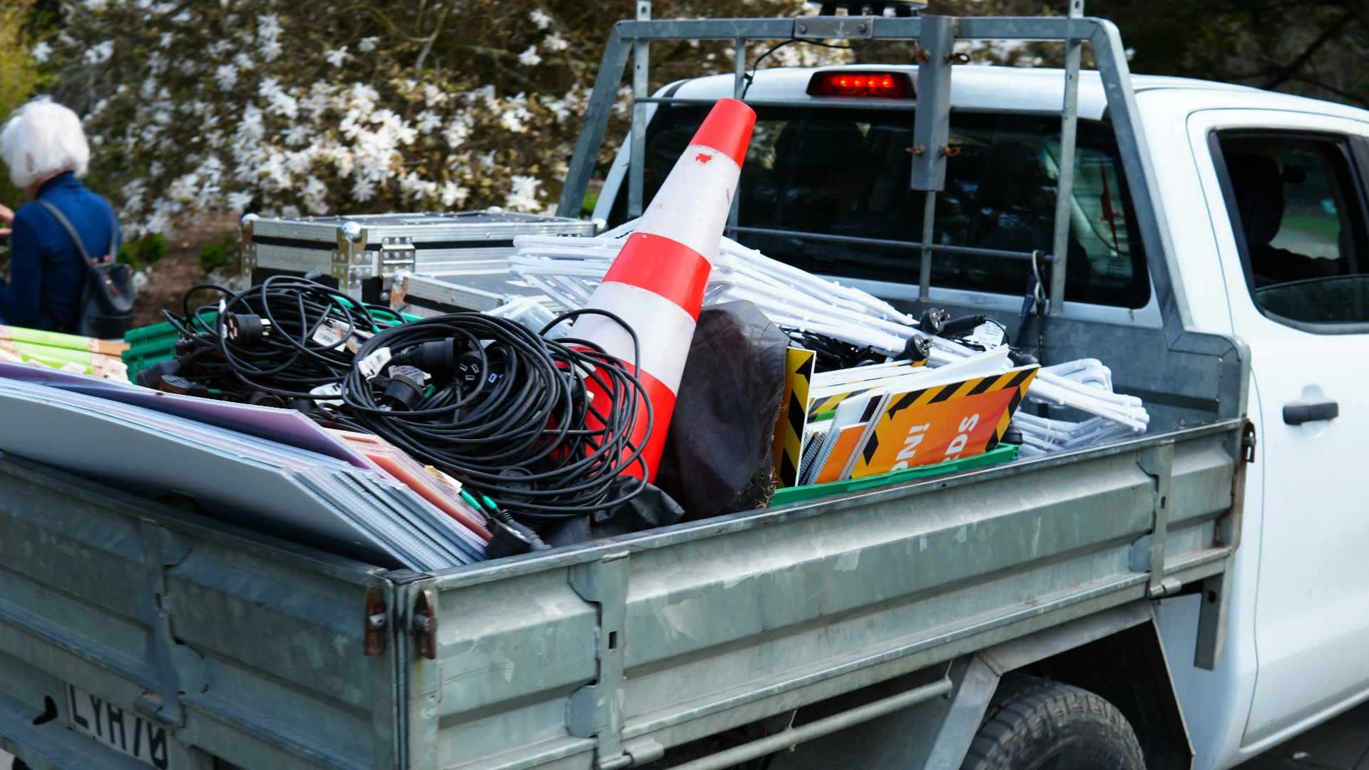 A white pickup truck bed filled with electrical cables, a traffic cone, and signs