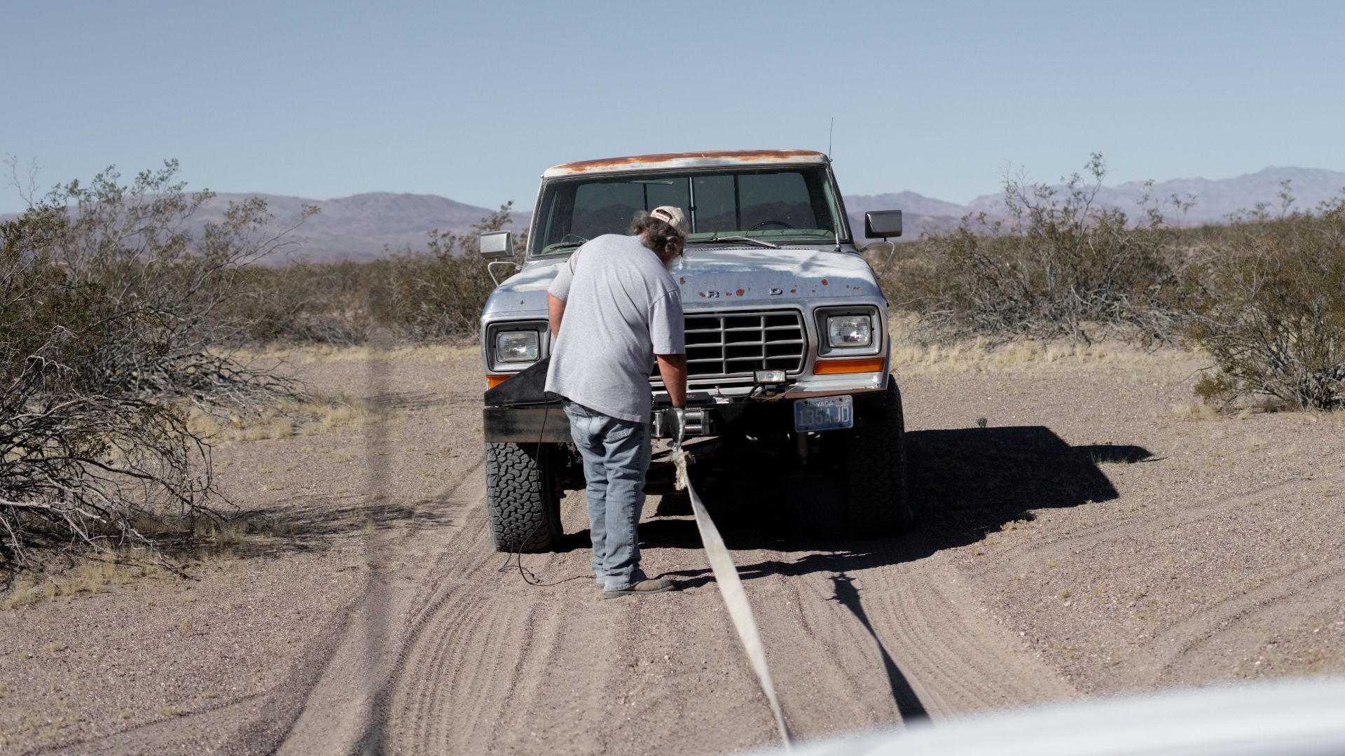 Man assisting stranded pickup truck in arid desert setting.