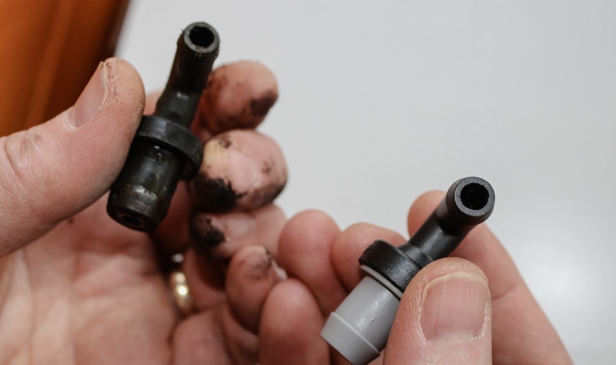 A person holding an old Positive Crankcase Ventilation (PCV) valve shown by a new one. Automotive design element.