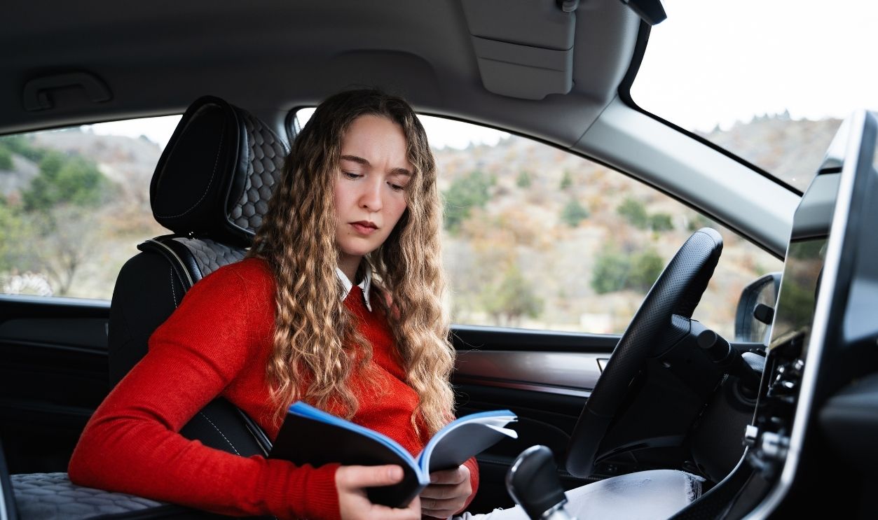 A young puzzled woman reads the car manual because of a problem with the new car. A worried female driver in casual wear reading the owner's manual of her auto. Buy or rent an automobile.