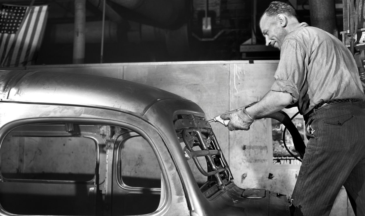 Factory worker drilling and bolting operation, all done by rapid and accurate automatic tools, on body of Dodge Army truck, Chrysler Corporation Dodge truck plant, Detroit, Michigan, USA, Arthur S. Siegel, U.S. Office of War Information, August 1942. 
