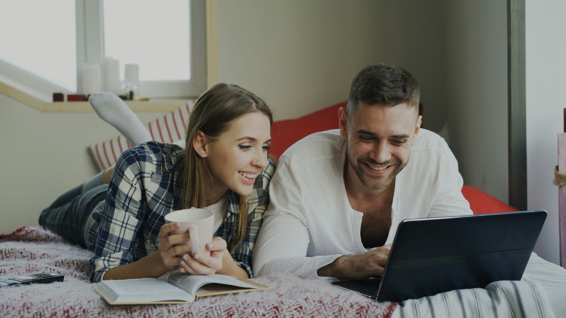 Couple lying on bed with laptop and coffee