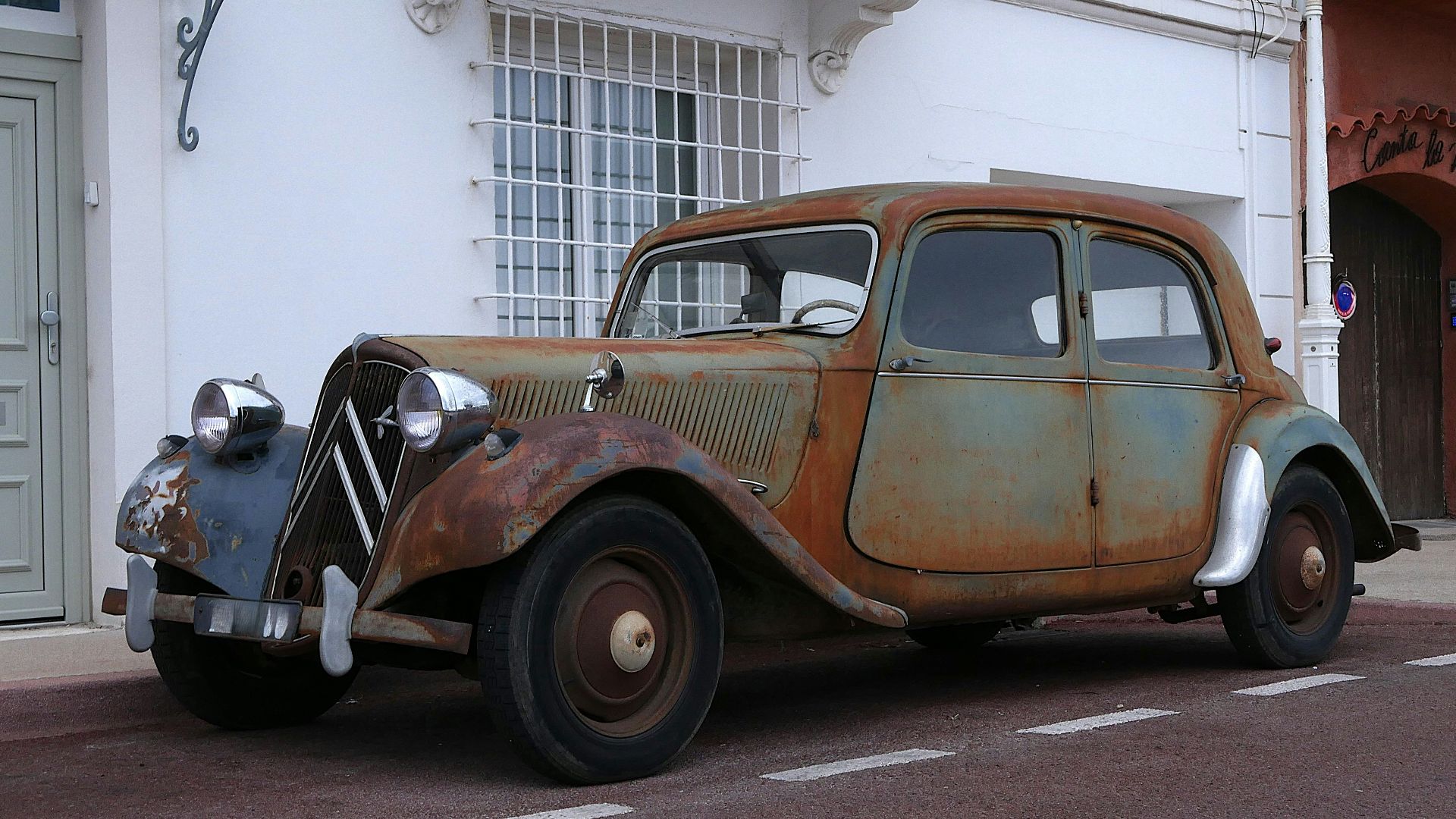 An old rusty car parked on the side of the road