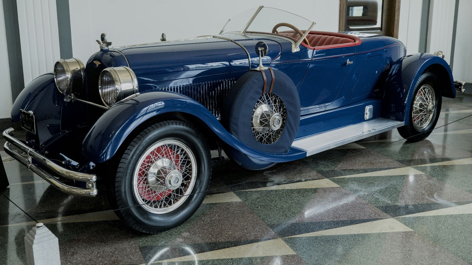 A dark blue vintage car with red interior parked indoors.