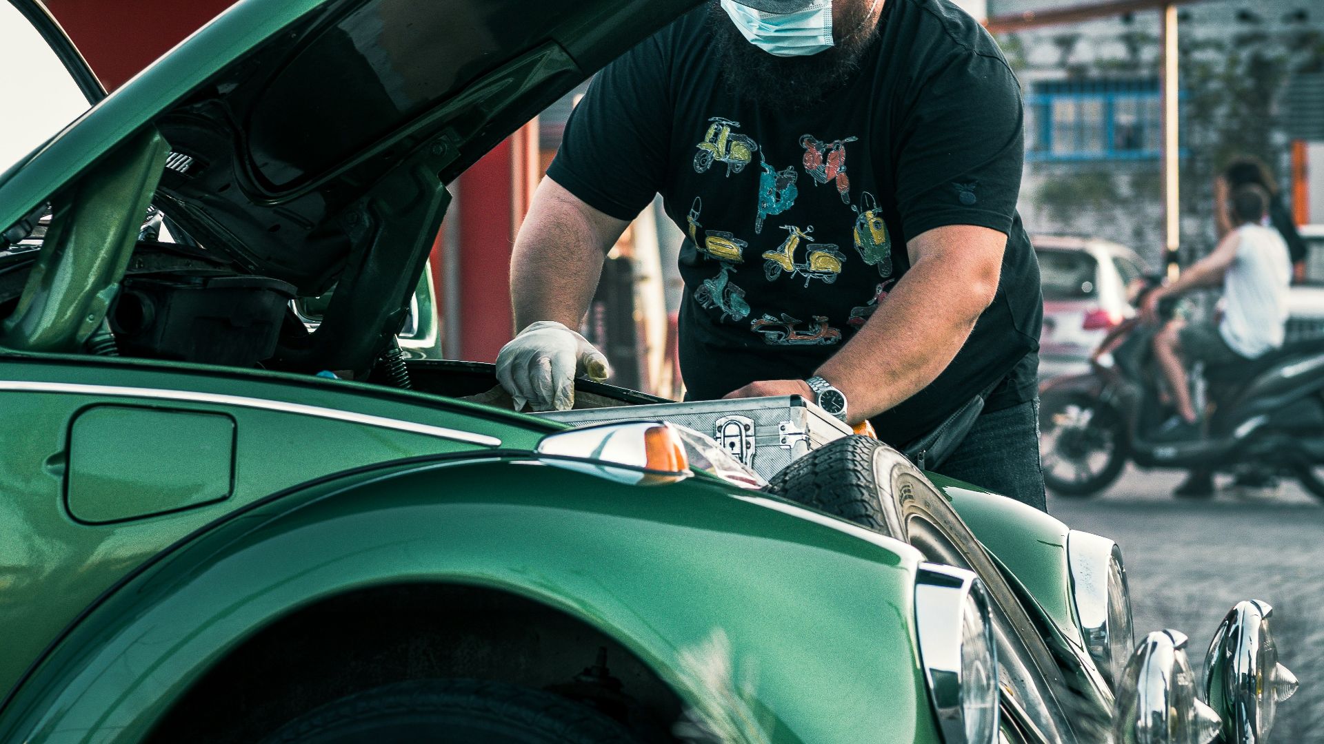 man in black t-shirt and white pants standing beside green car