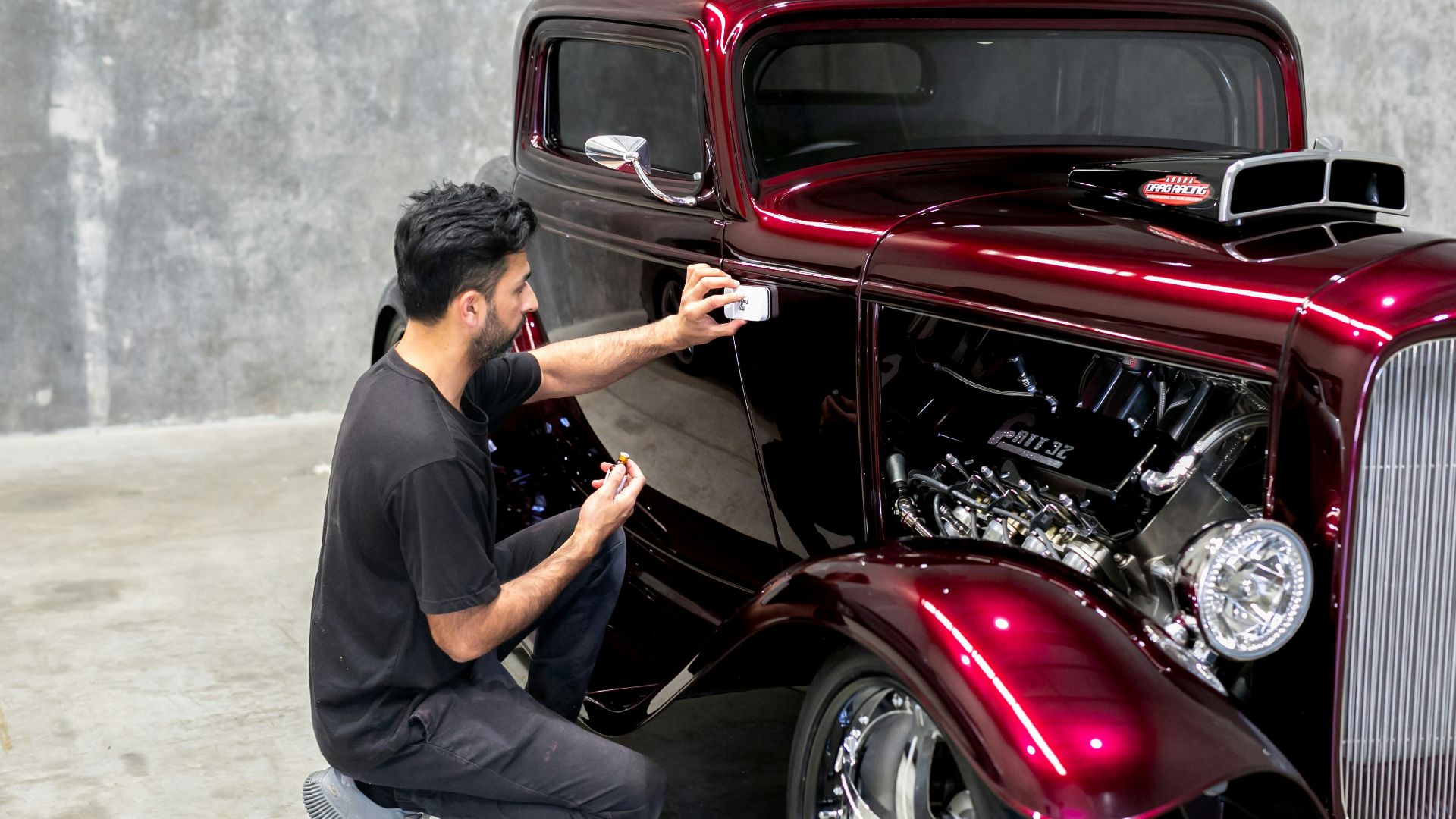 Man takes a photo of a shiny, red hot rod.