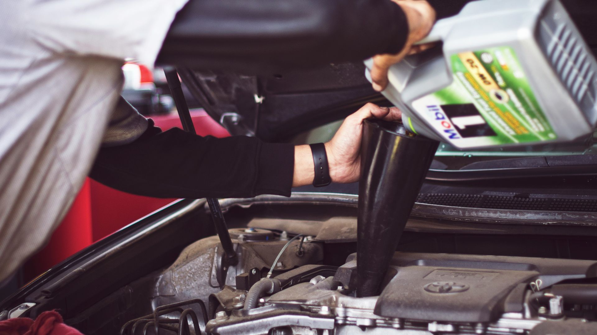 man refilling motor oil on car engine bay