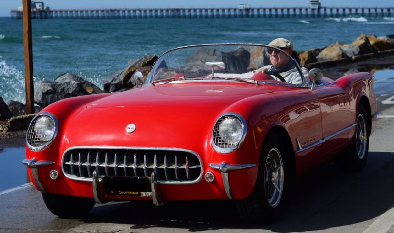 Vintage red Chevrolet convertible driven along a scenic seaside road