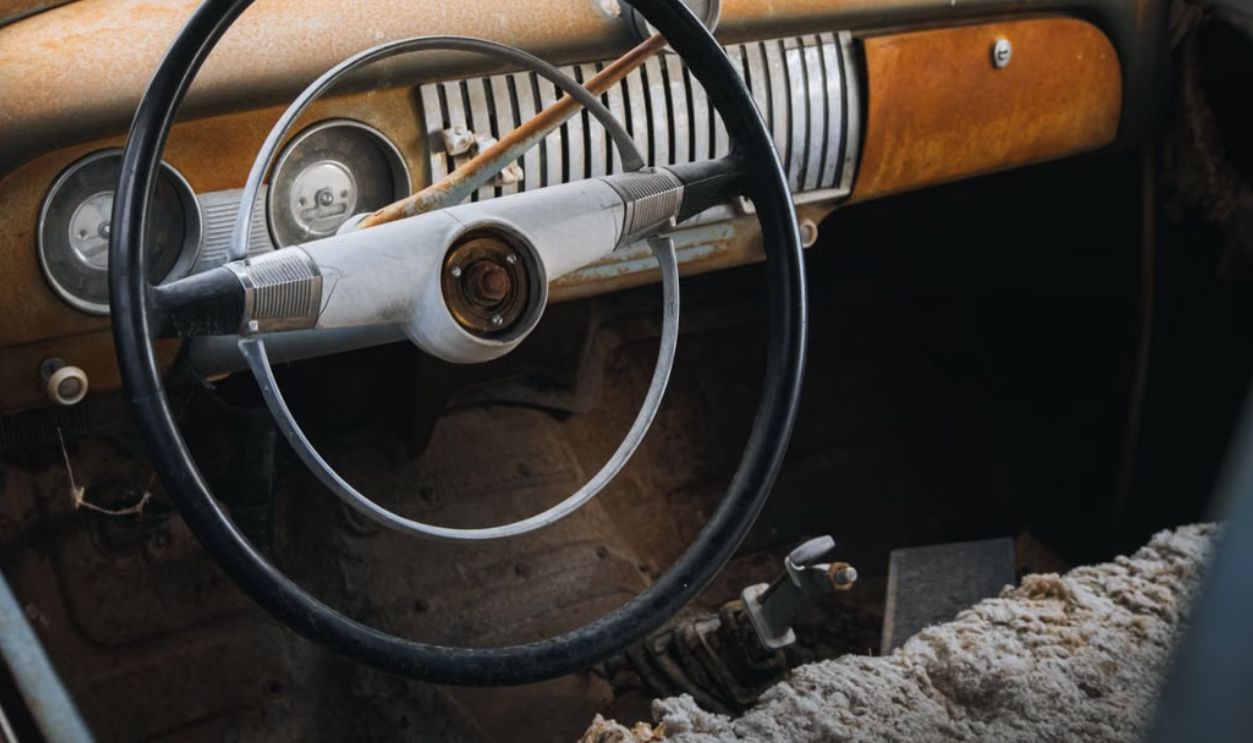 Close-up of a vintage car's interior, featuring a rusted dashboard and classic steering wheel