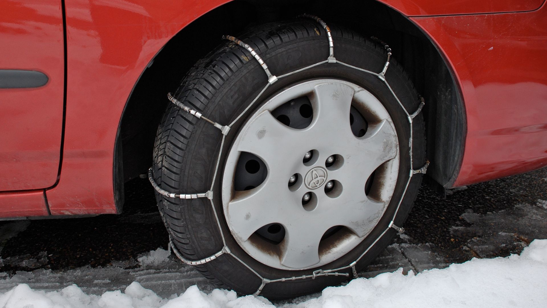 Radial-type cable chains on a car tire.  (The car here is a Toyota Corolla, which has front-wheel drive, and the photo was taken in Portland, Oregon.)