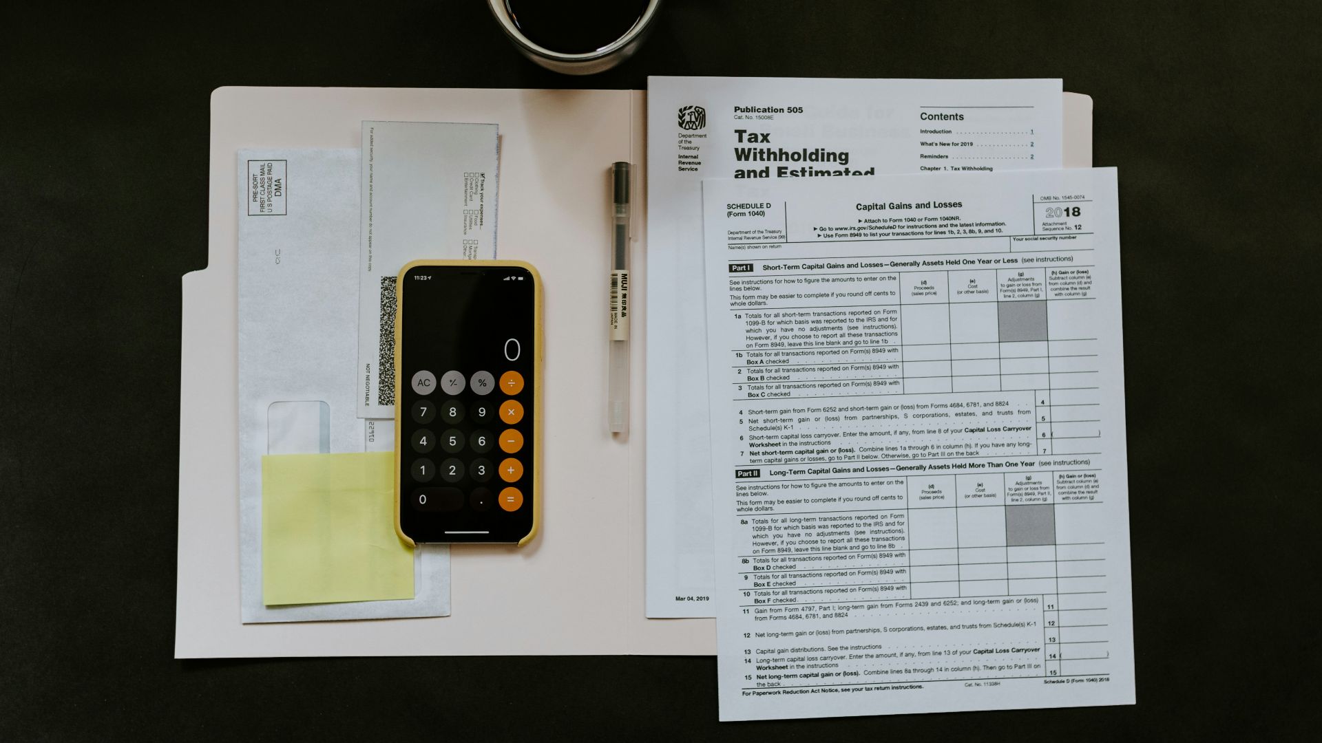 black Android smartphone near ballpoint pen, tax withholding certificate on top of white folder