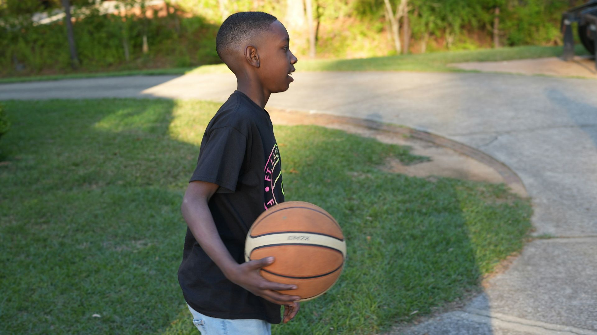 a young boy holding a basketball on a street