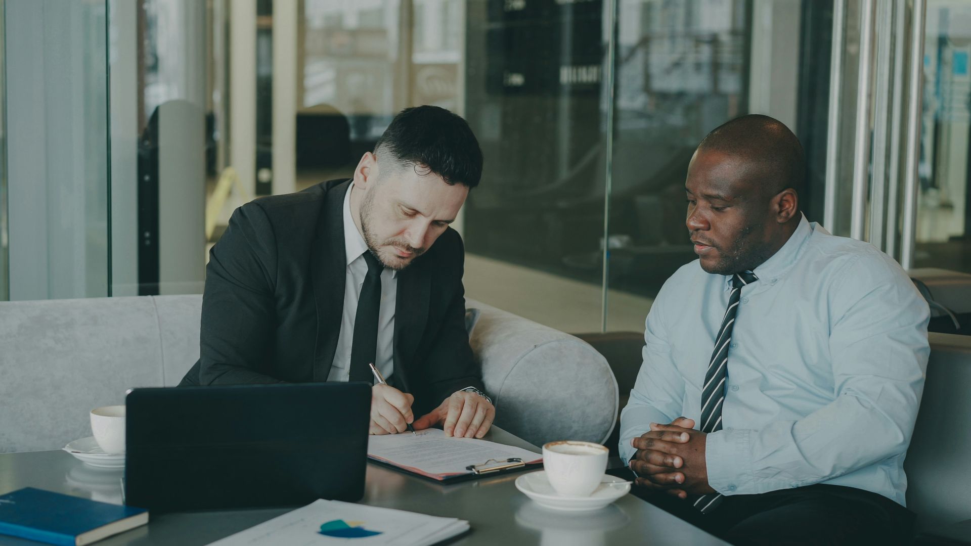 Two businessmen signing a document at a table
