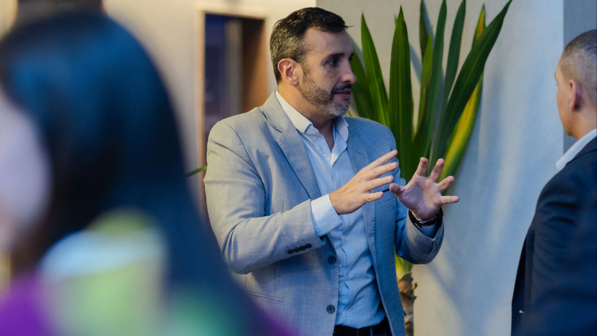 A man in a suit gestures while talking indoors