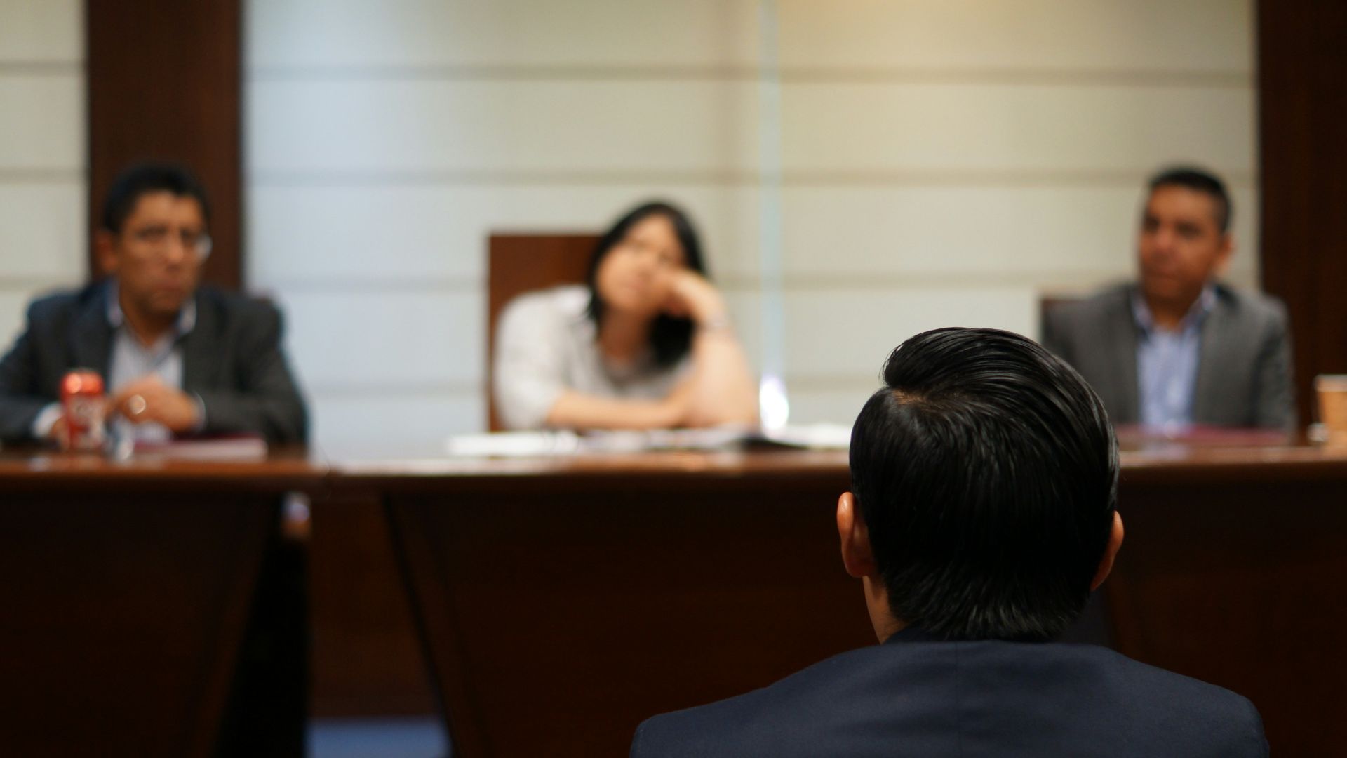 A person in a suit facing three people seated at a long wooden table