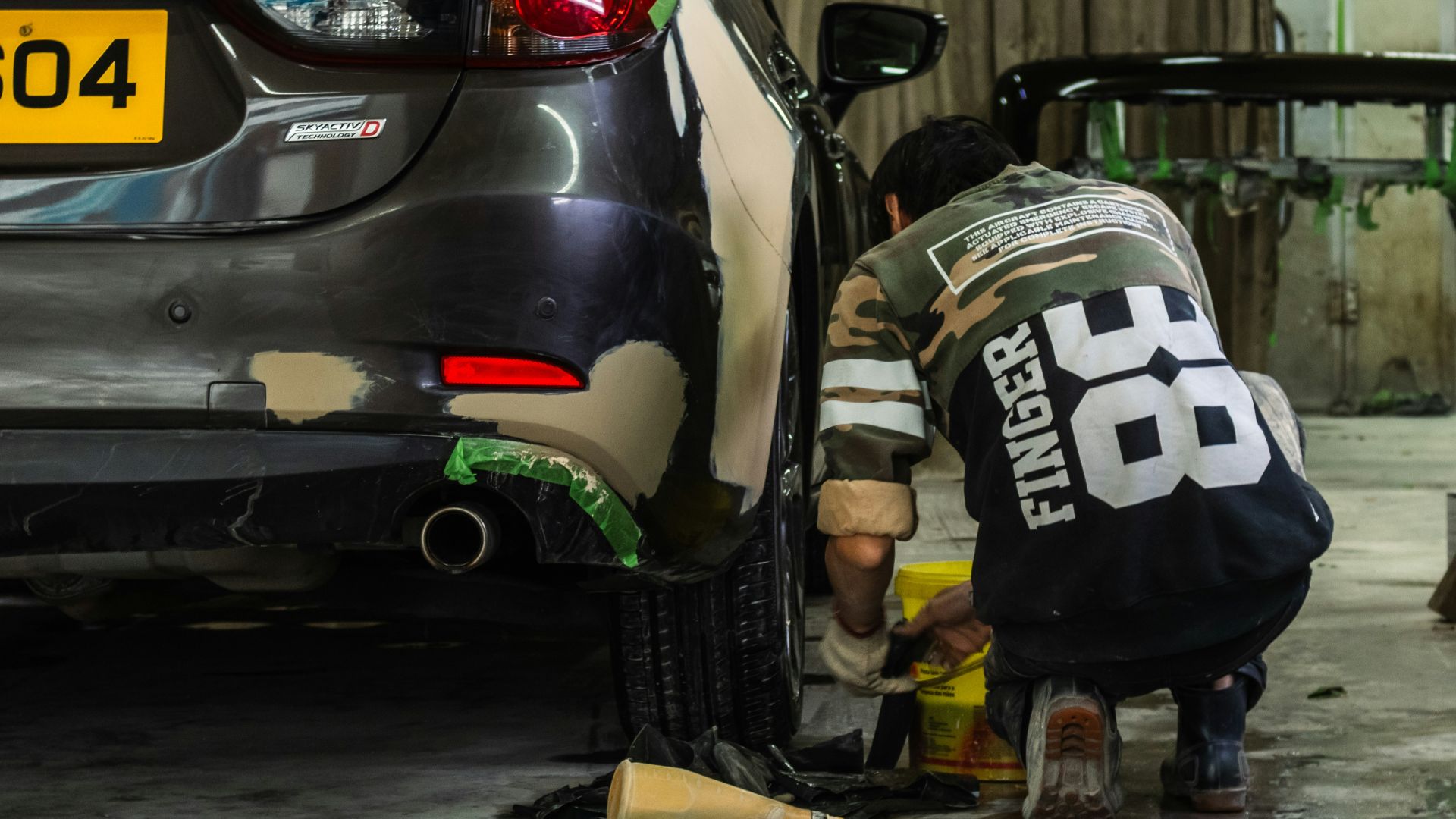 A person in a camouflage shirt repairing a car bumper in a workshop