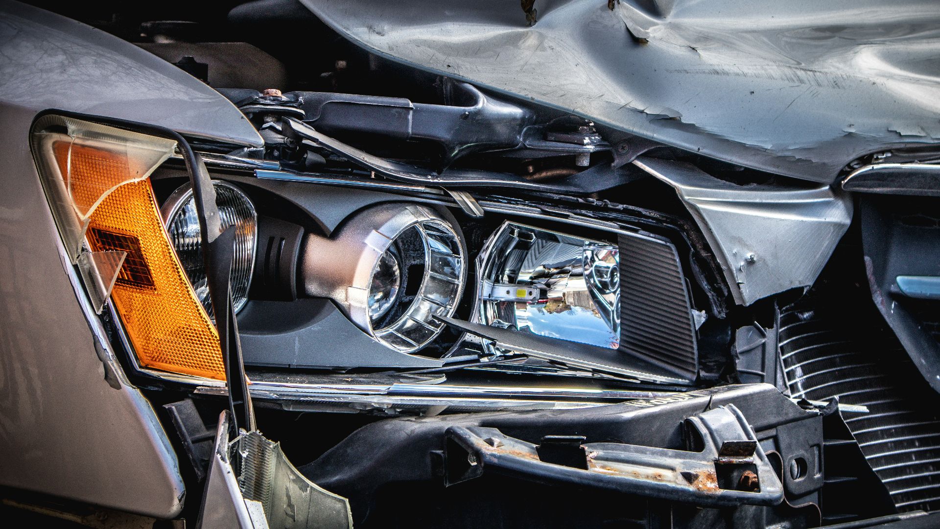 A damaged silver car with a crushed hood and broken headlight assembly