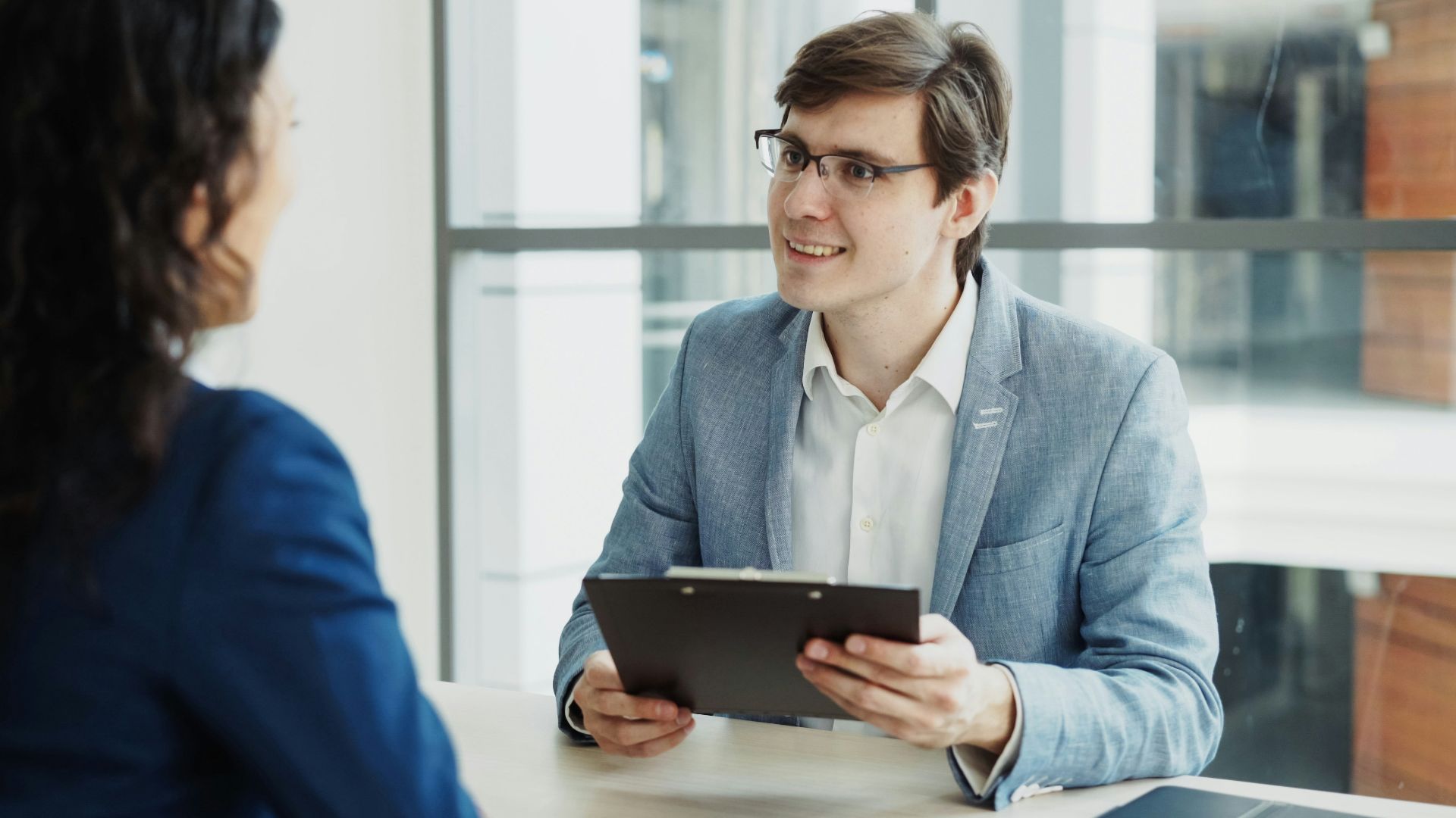 Man in suit interviews woman holding clipboard