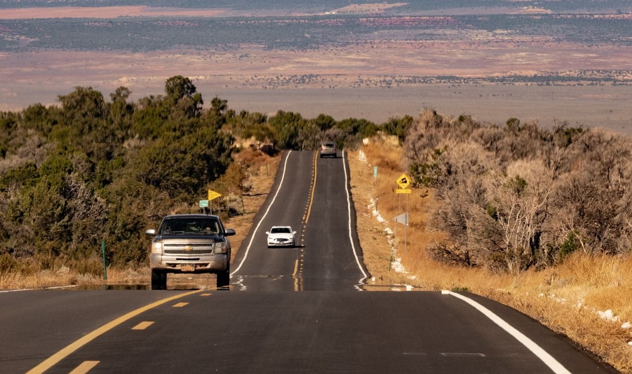 Long desert highway with cars against vibrant red rock canyons under a vivid blue sky