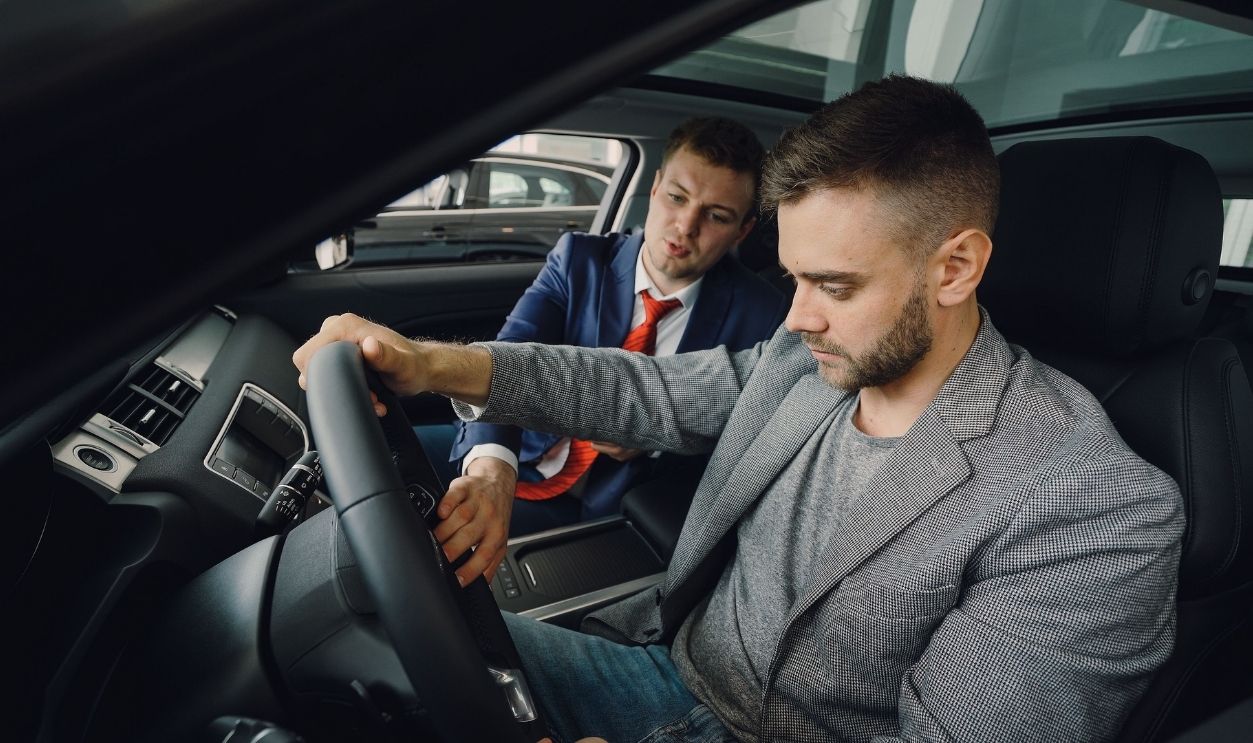 Salesman demonstrating car features to potential buyer inside vehicle