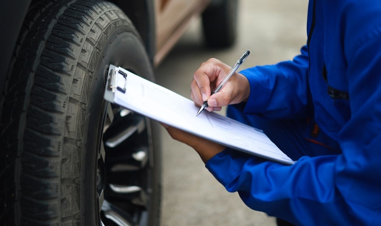 Auto mechanic is writing on clipboard. Mechanic is making checklist and checking condition of car tire. Concept of car service, repair, maintenance.