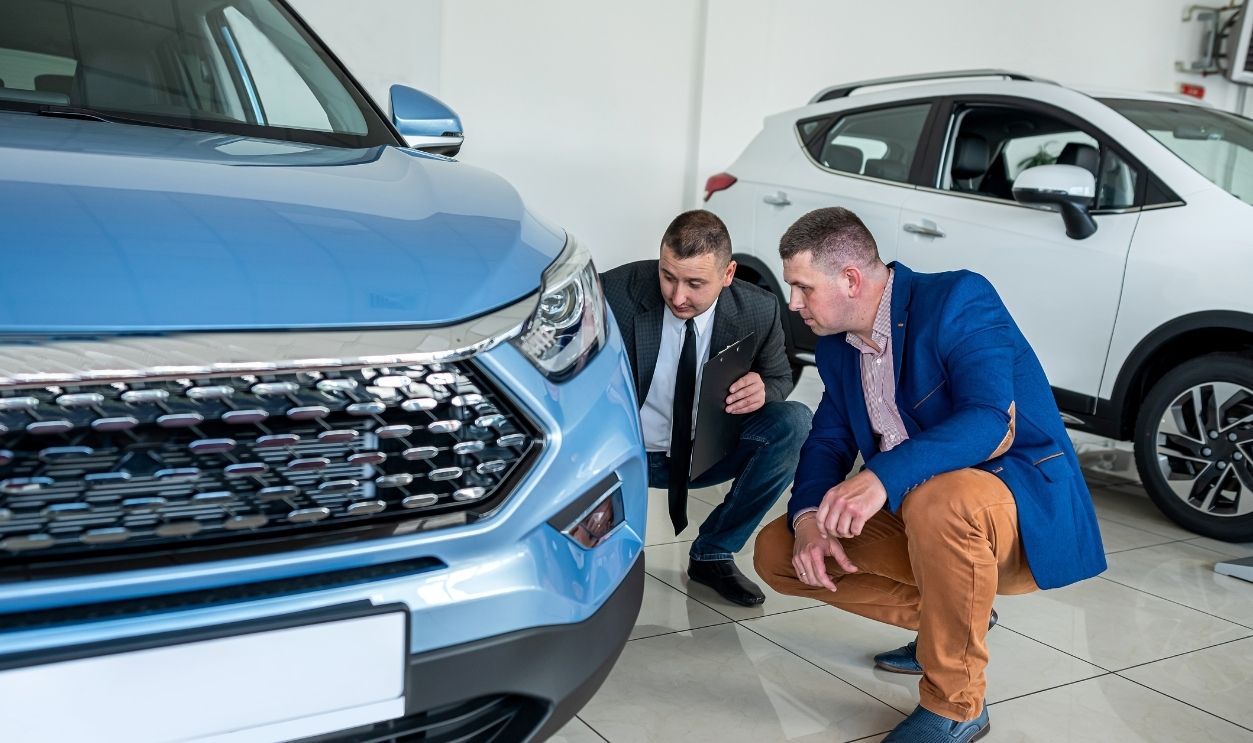 Young professional manager and male client choosing and examining a new auto before purchase in dealership
