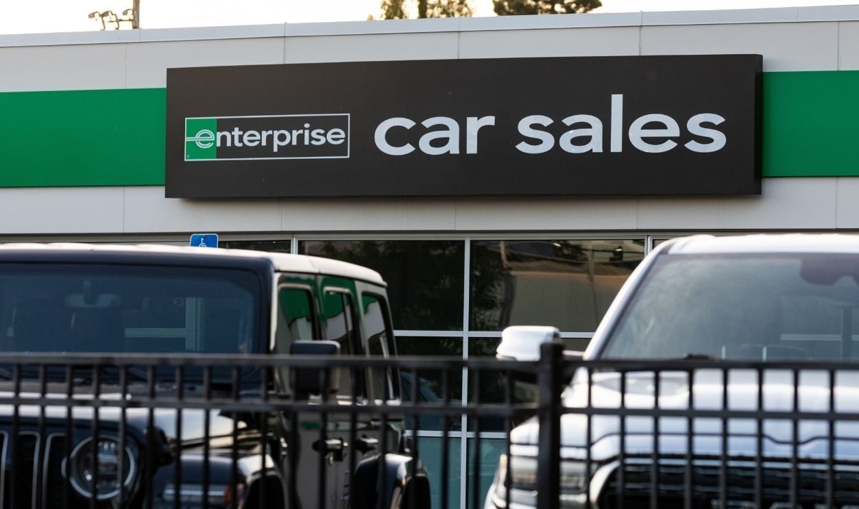 Beaverton, OR, USA – May 24, 2025 – Enterprise Car Sales storefront with bold black and green signage above large windows. Jeep Wrangler and Dodge Ram vehicles are parked in front of the building