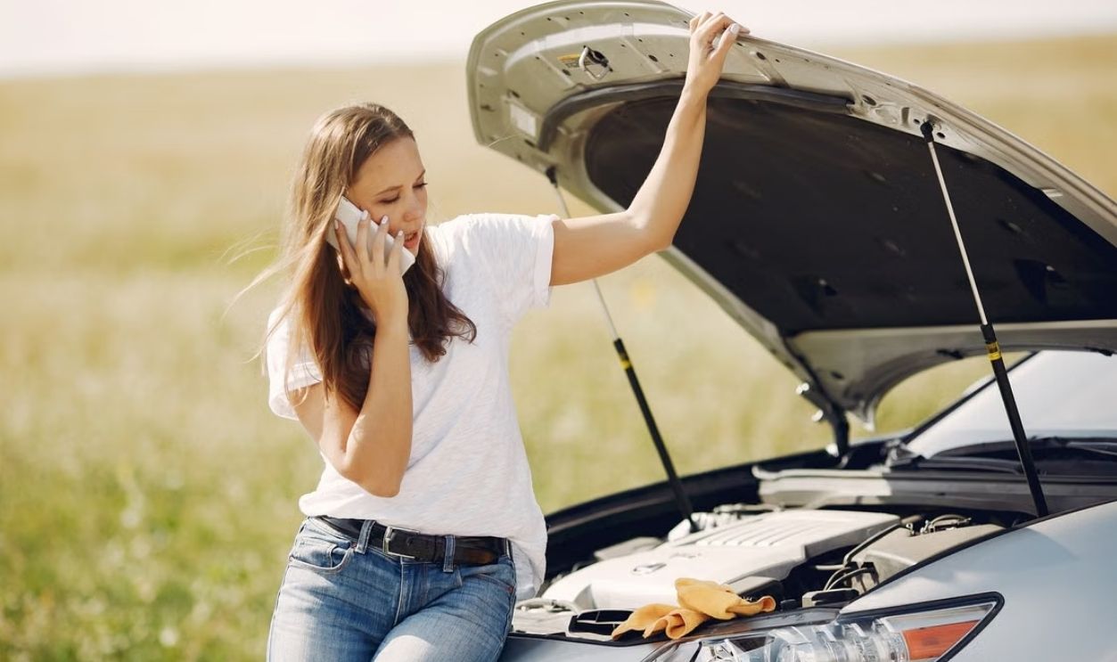 Young woman on phone seeking help for car breakdown on a sunny day.