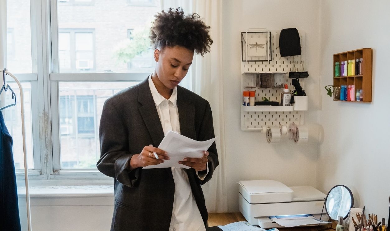 Woman in a home office setting reading documents with a laptop on the desk.