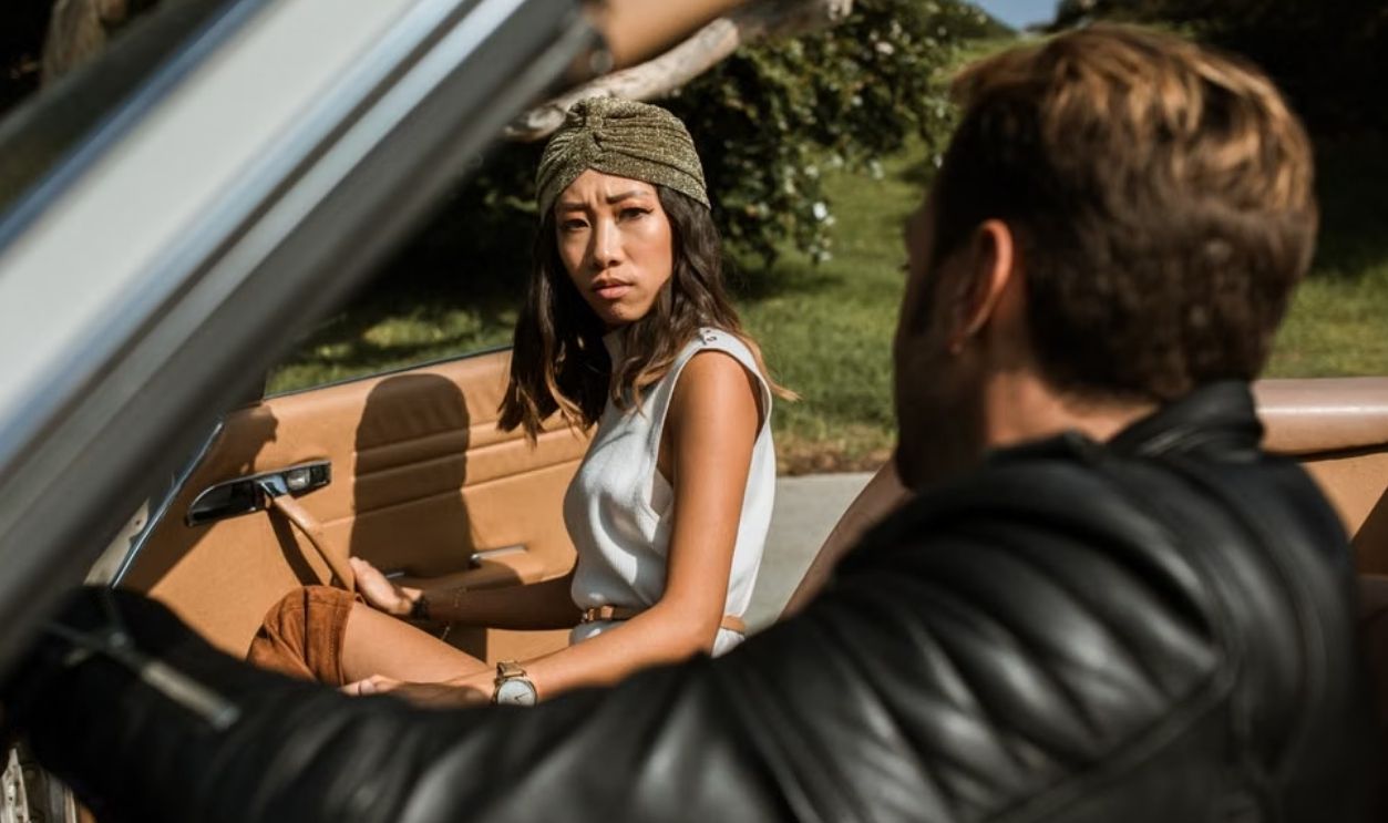 A couple having an intense conversation while seated in a convertible car outdoors.