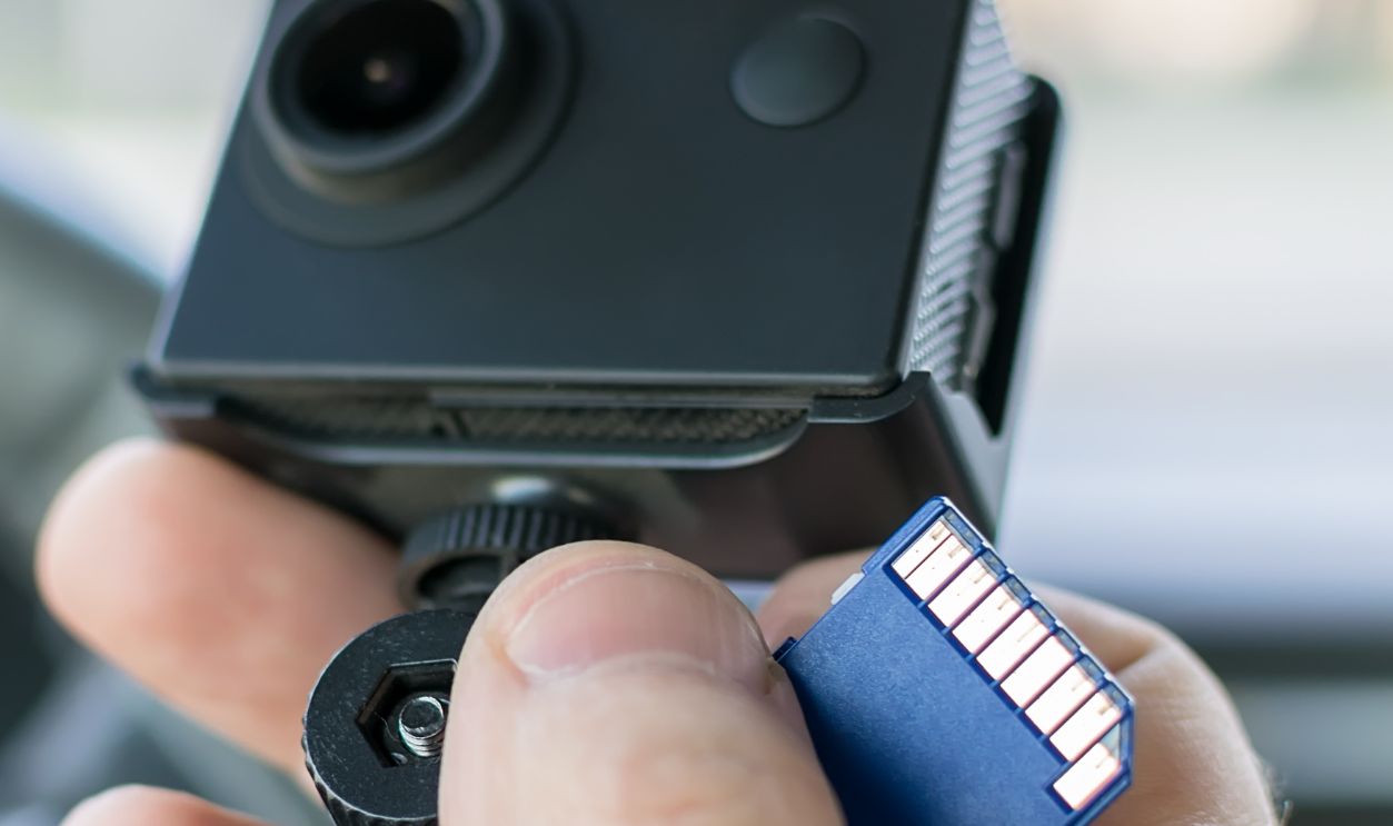 the hand of a male car driver that holds a car DVR recording incidents and a memory card to it