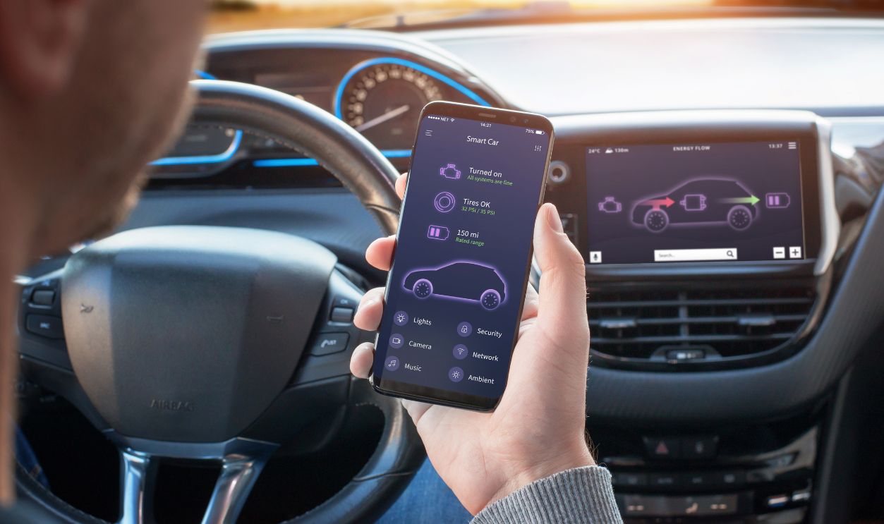Smart Car app with engine, tyres and battery status information concept. Driver holds a mobile phone. Steering wheel and board display in the background