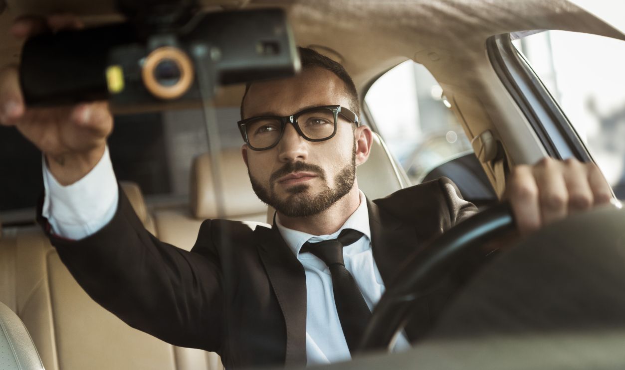 handsome driver in suit driving car and fixing mirror