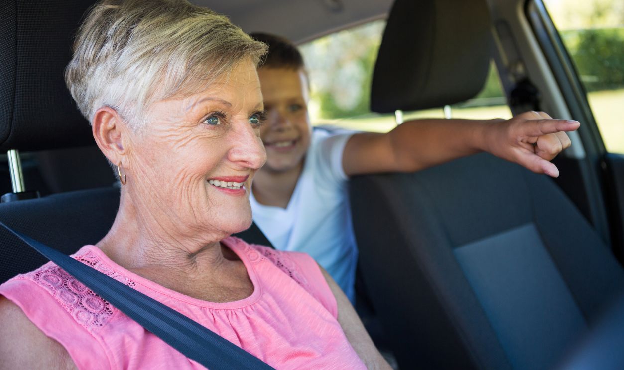 Grandmother driving a car while grandson sitting in the back seat of car
