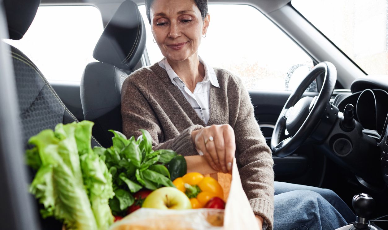 Shutterstock-2371016763, Portrait of smiling adult woman with grocery bag in car, copy space