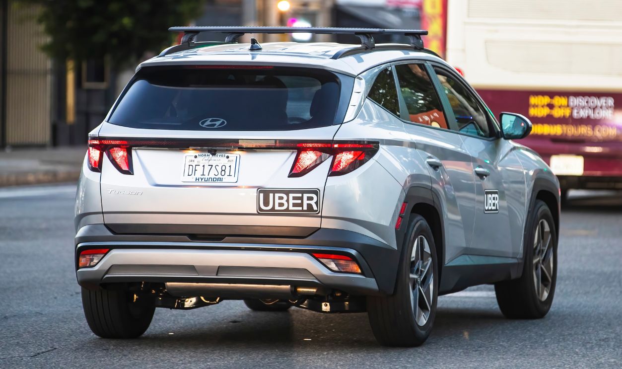 2024-11-15 Los Angeles USA Silver Hyundai Tucson with Uber decals, driving on a Los Angeles street, captured in an urban traffic setting with a bus in the background.